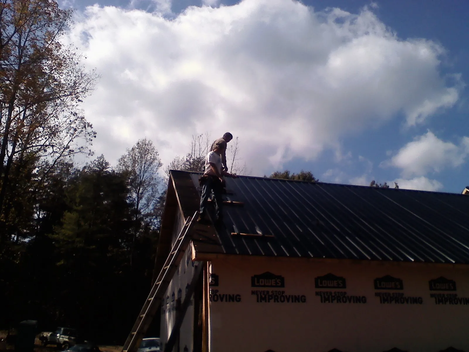 Roofer fastening dark metal panels high against a cloudy sky, from a Roof Inspection job in Houston